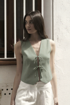 Sage green linen vest top with V-neck and tie front detail, paired with white trousers