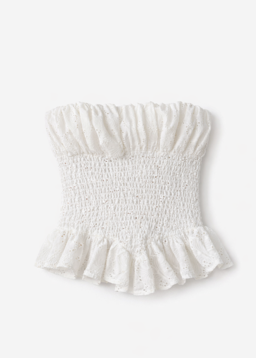 White smocked eyelet lace tube top with ruffle trim at top and bottom hem on neutral background