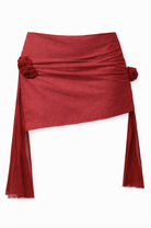 Red linen mini skirt with asymmetric hem, gathered rosette details at sides, and flowing sheer mesh panel extensions