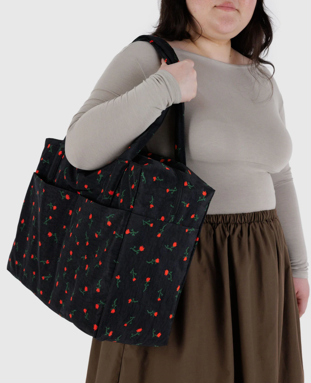 Black tote bag with red rose print pattern being carried on shoulder, featuring exterior pockets and sturdy straps