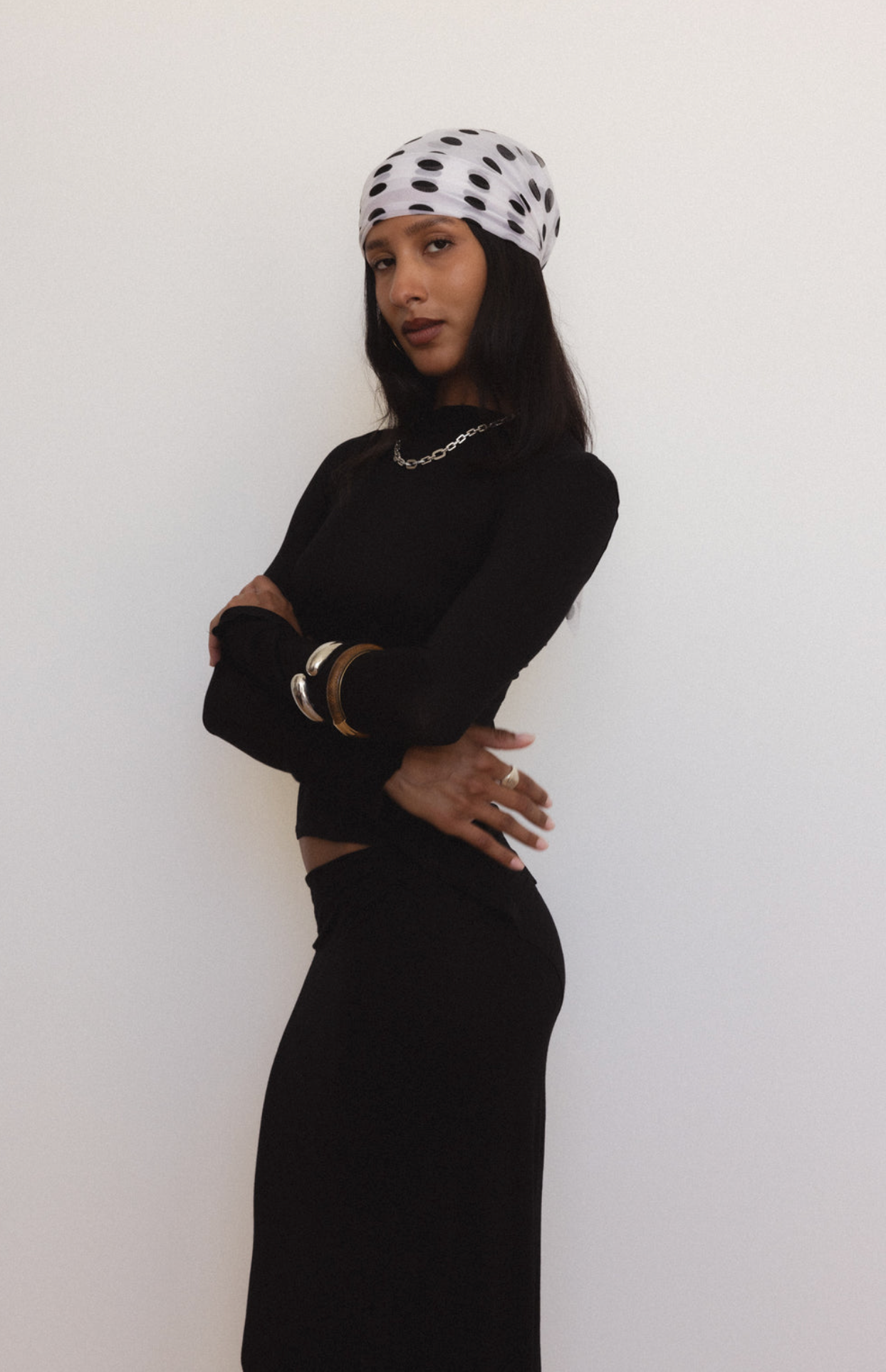 Woman wearing white polka dot beanie hat with black spots, styled with black outfit and silver jewelry against neutral background