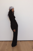 Woman wearing all-black knit outfit with polka dot mesh veil headpiece against white wall