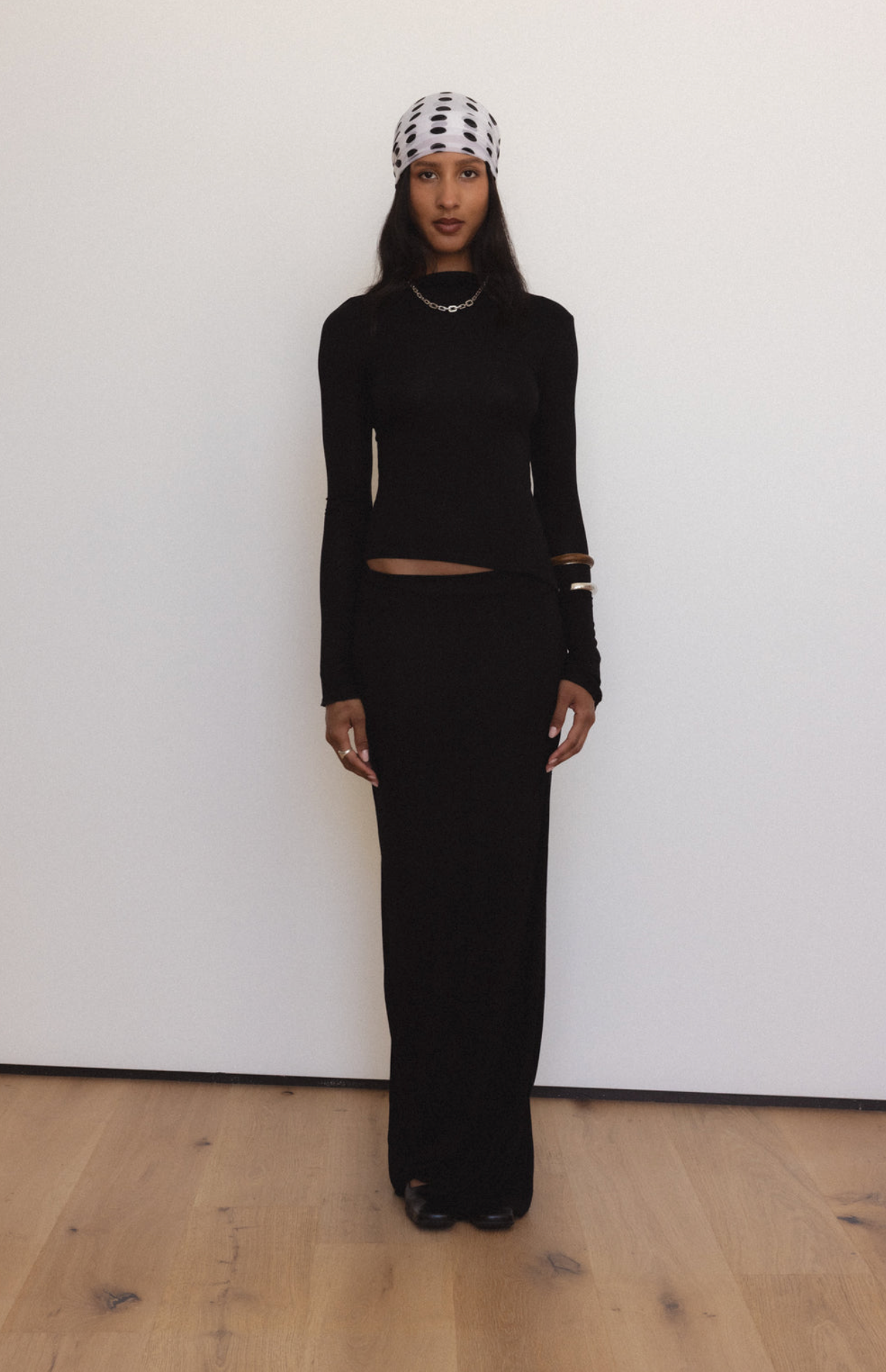 Black knit two-piece set with long-sleeve crop top and maxi skirt, styled with polka dot beanie and chain necklace