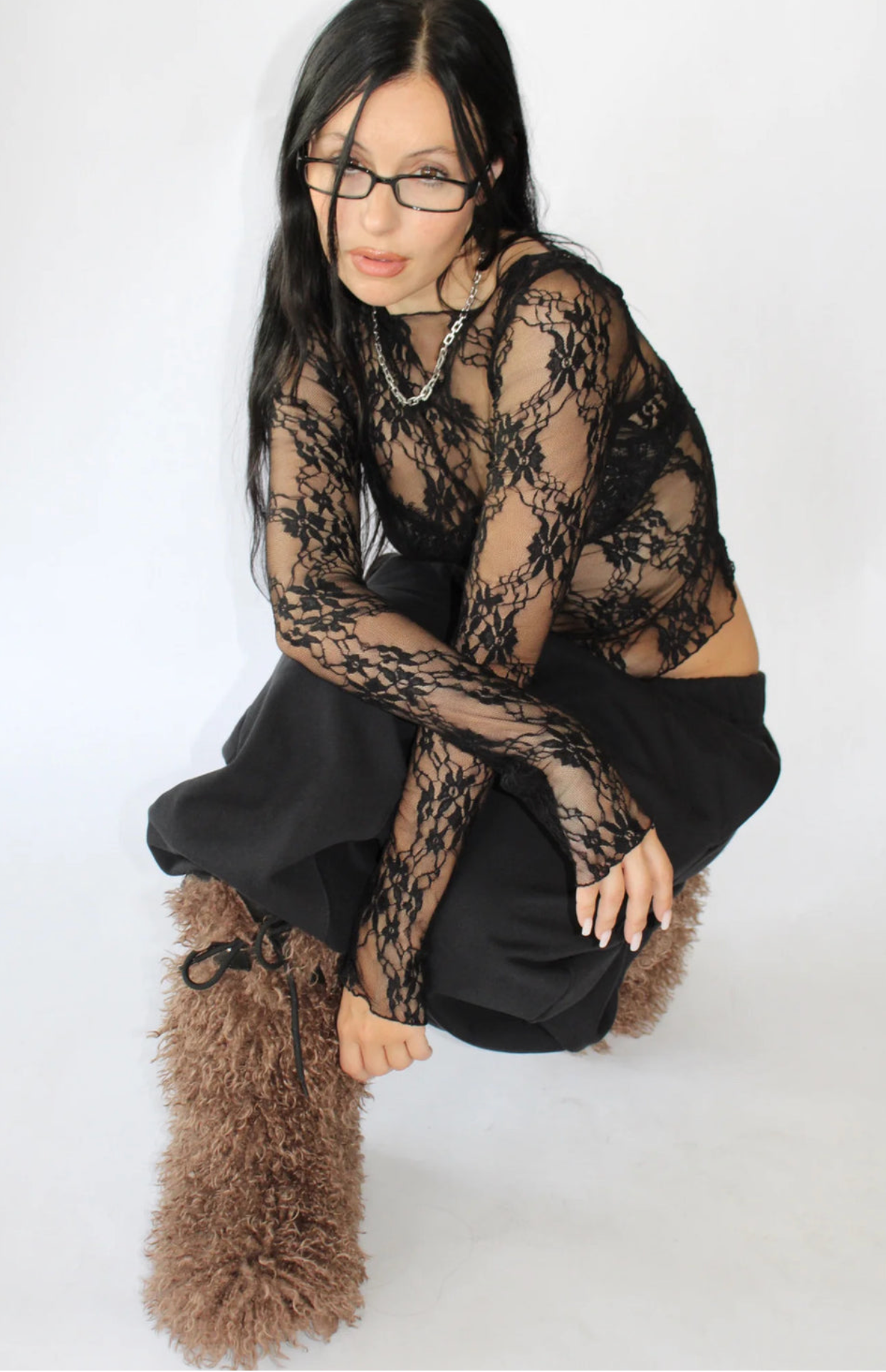 Person wearing black lace long-sleeve top with floral pattern, black pants, and tan fuzzy boots against white background