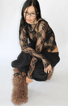 Person wearing black lace long-sleeve top with floral pattern, black pants, and tan fuzzy boots against white background