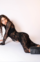 Black lace jumpsuit with long sleeves and sheer floral pattern, worn by model with curly hair and black boots
