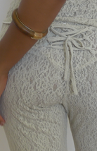 White lace long-sleeve blouse with tie-neck detail and delicate floral pattern, worn with gold collar necklace