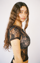 Black lace short sleeve bodysuit with floral pattern and sheer mesh detailing, worn by model with long wavy hair
