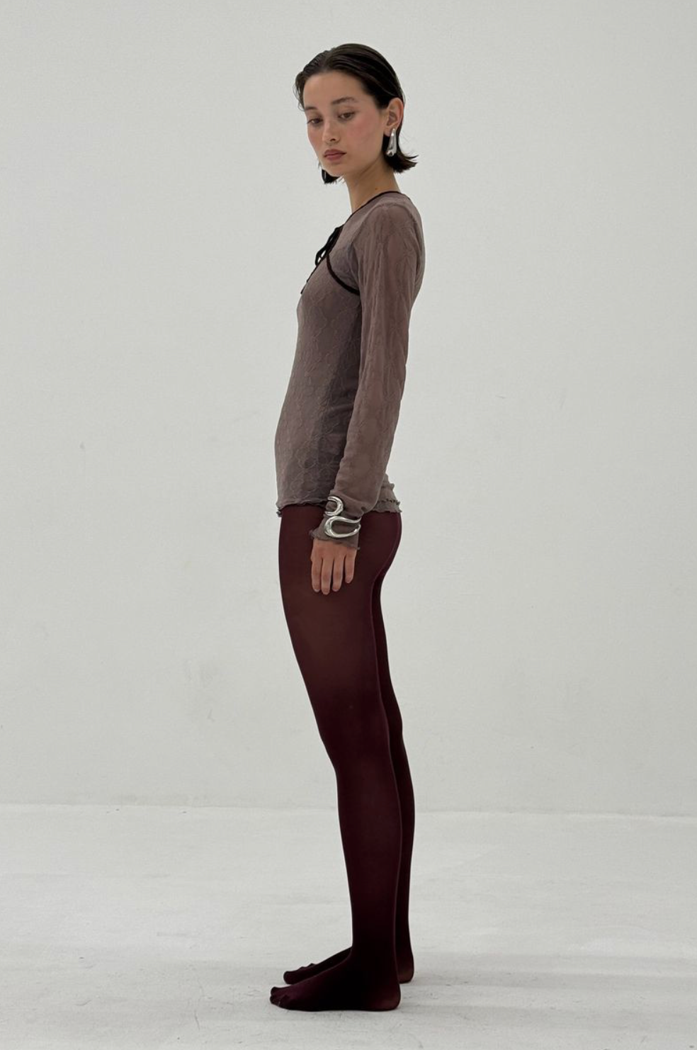 Woman wearing burgundy ribbed tights and taupe long-sleeve top, side view showing full-length fit and texture