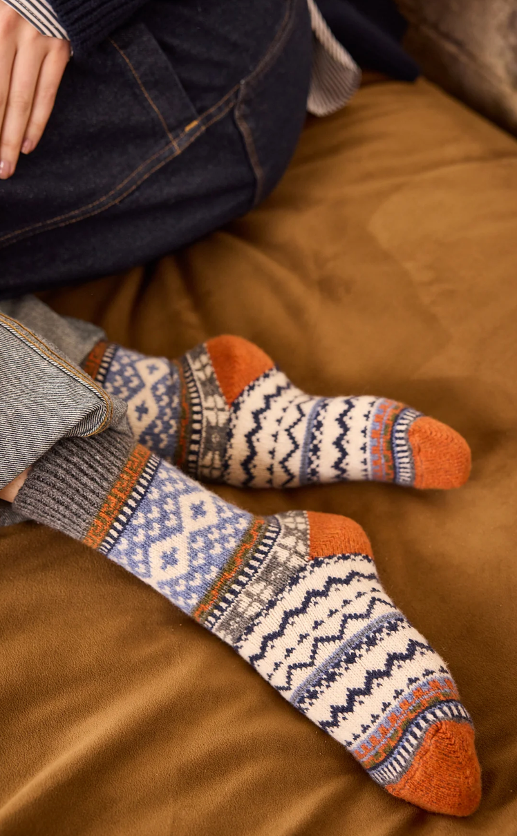 Colorful knit socks with Fair Isle patterns in cream, blue, gray, and orange tones with orange heels and toes