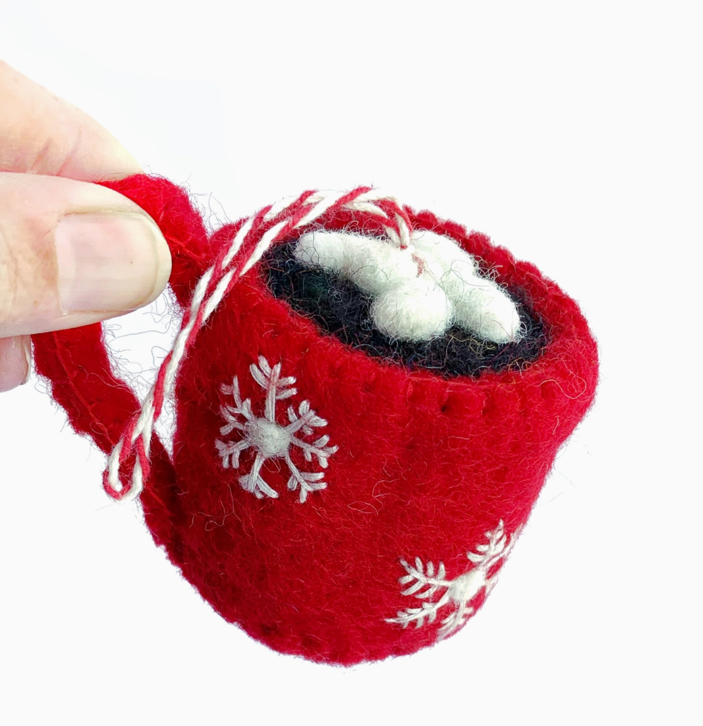 Red felt mitten ornament with white snowflake details and black/white pom-pom decoration inside, held by hand