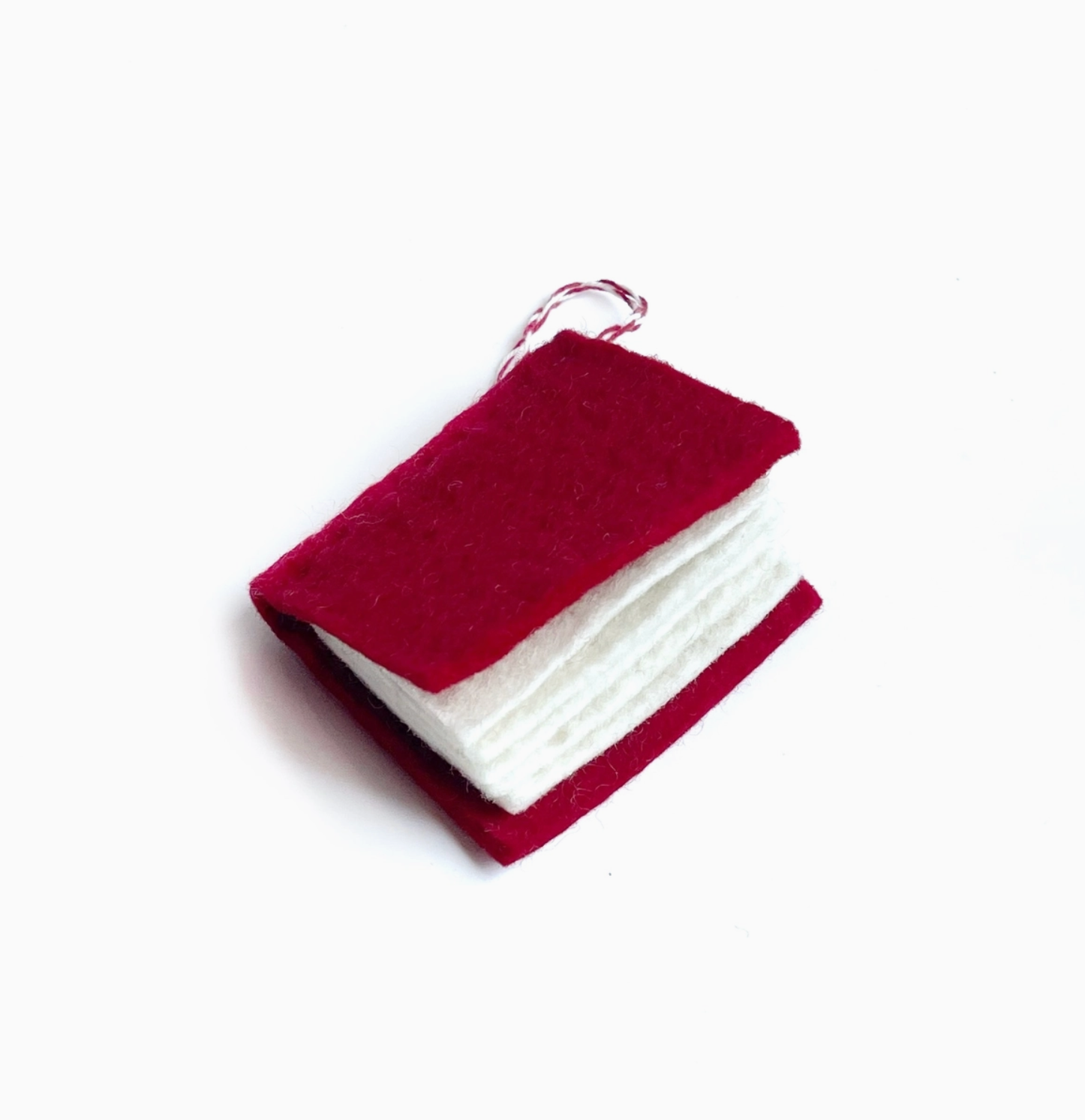 Miniature red and white felt book ornament with twisted string loop hanger on white background