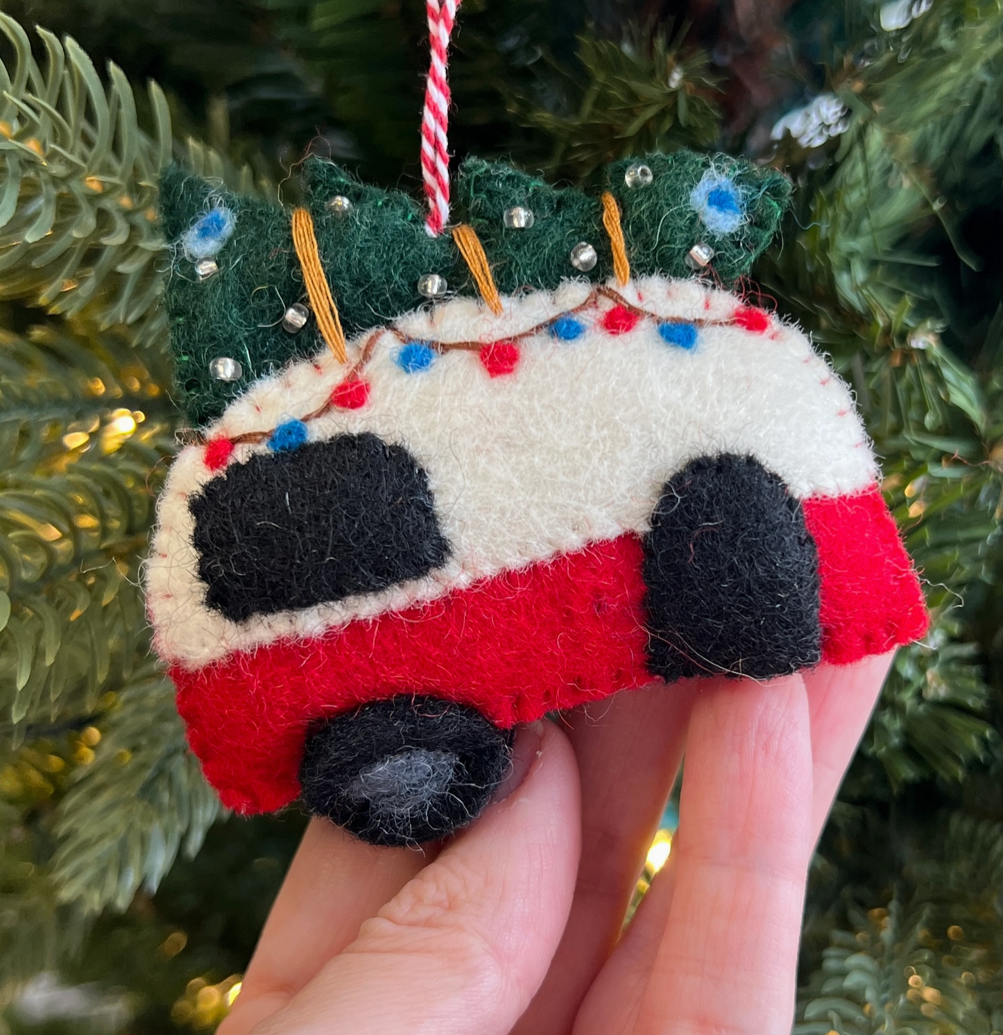 Handmade felt Christmas ornament of a red and white camper van with black wheels, decorated tree on roof, hanging from tree