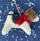 Handmade felt dog ornament in cream with brown ears, black saddle marking, and red collar with striped hanging cord