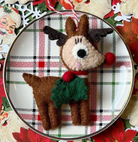 Felt reindeer ornament in brown with black antlers, green sweater, and candy cane string on plaid holiday plate
