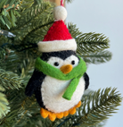 Handmade felt penguin ornament with Santa hat and green scarf hanging on Christmas tree branches