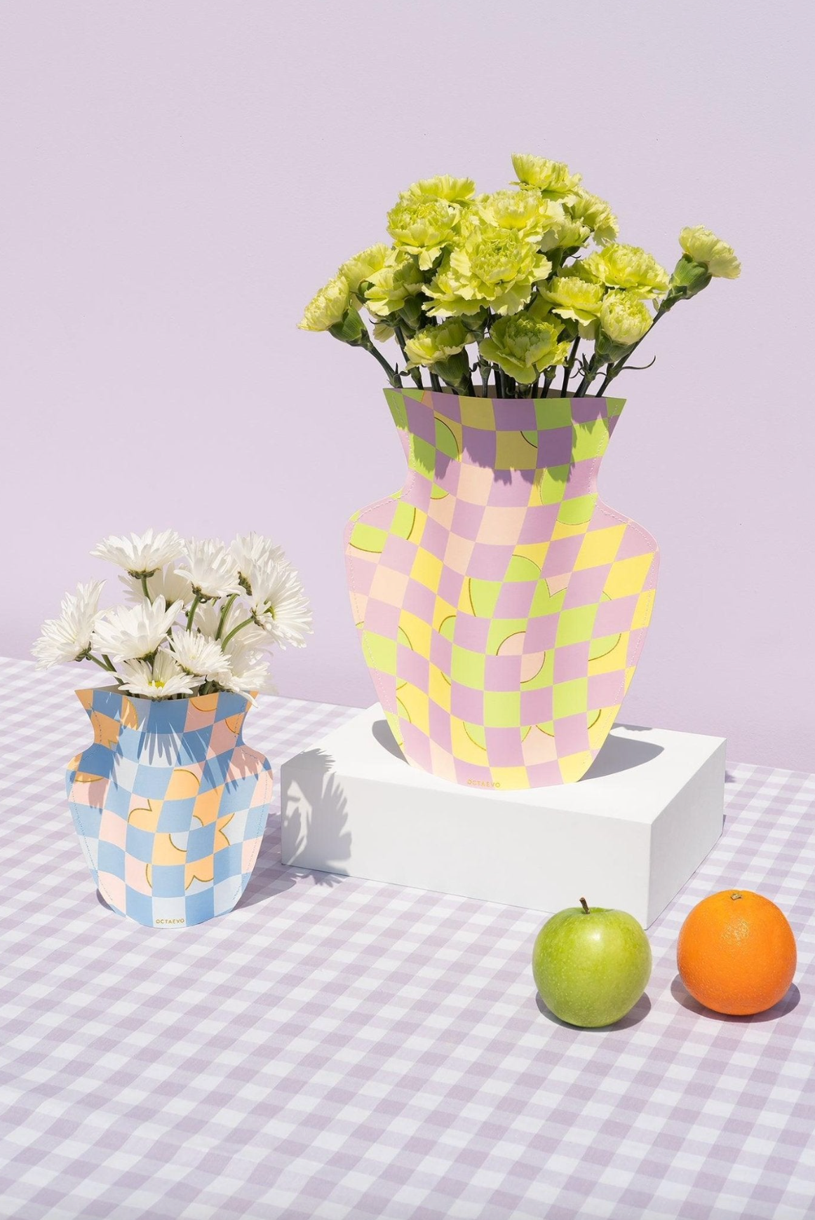 Colorful checkered paper vases in pastel pink, yellow, and blue patterns holding fresh flowers on gingham tablecloth