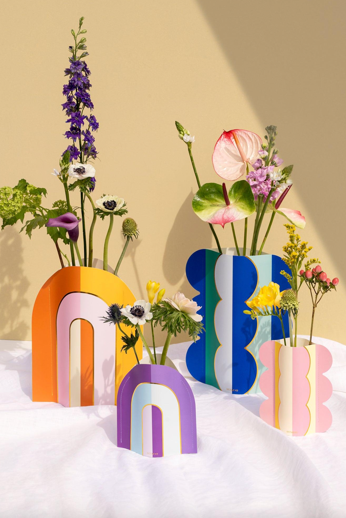 Colorful geometric vases with arch and wavy designs in pink, purple, yellow, and blue holding fresh flower arrangements