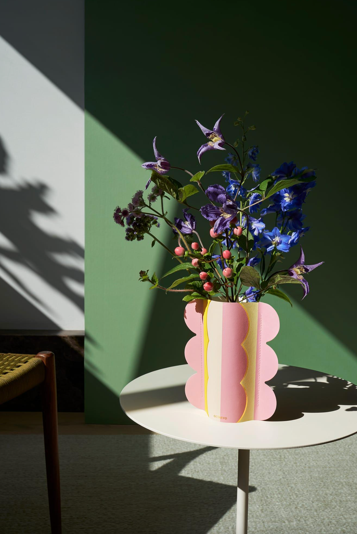 Pink and cream scalloped paper vase with wildflowers on white round table against green wall