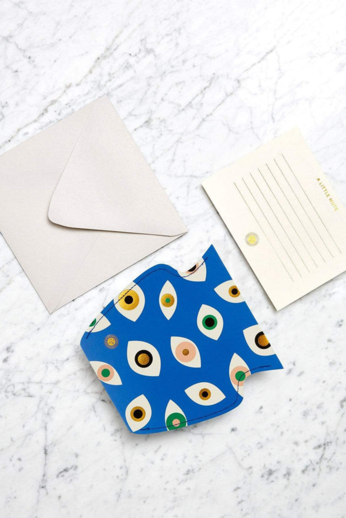 Blue eye pattern greeting card with matching cream envelope and postcard on marble surface