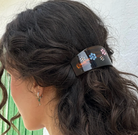 Dark tortoiseshell hair claw clip with colorful flower embellishments in pink, blue, and white holding back brown wavy hair