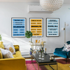 Three framed city neighborhood prints in blue, yellow, and light blue featuring local landmarks and phrases for Wilmington, Brooklyn, and Chapel Hill