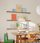 Wooden floating picture ledge shelf displaying colorful framed art prints in natural oak finish