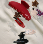 Assorted hair clips including red claw clip, star-shaped clips, and snap clips in various colors with glitter and rhinestone details