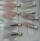 Pastel pink and lilac cloud-shaped hair clips with rhinestone details and silver metal clips, arranged on white fabric