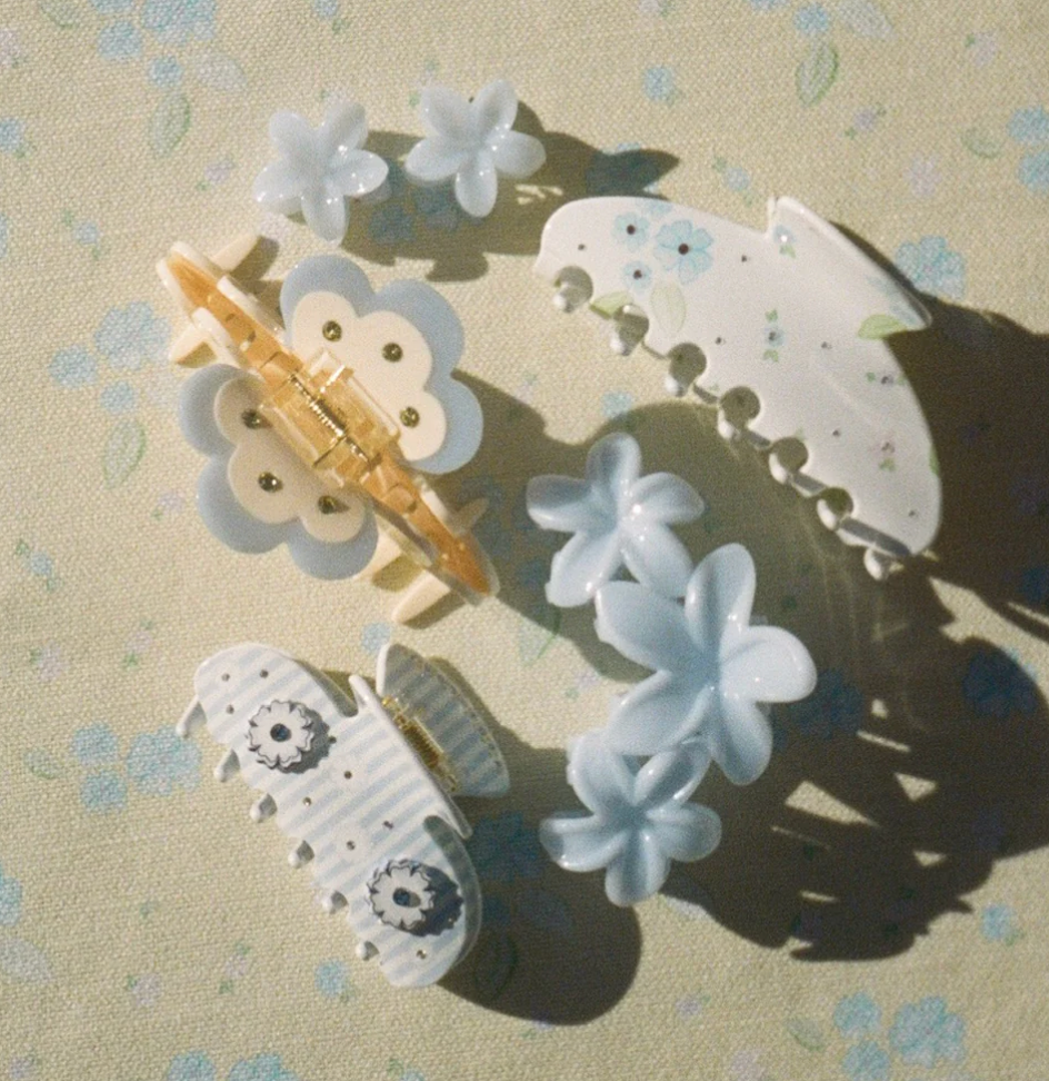 White and blue floral hair clips and barrettes with decorative dots and flower shapes on a floral fabric background