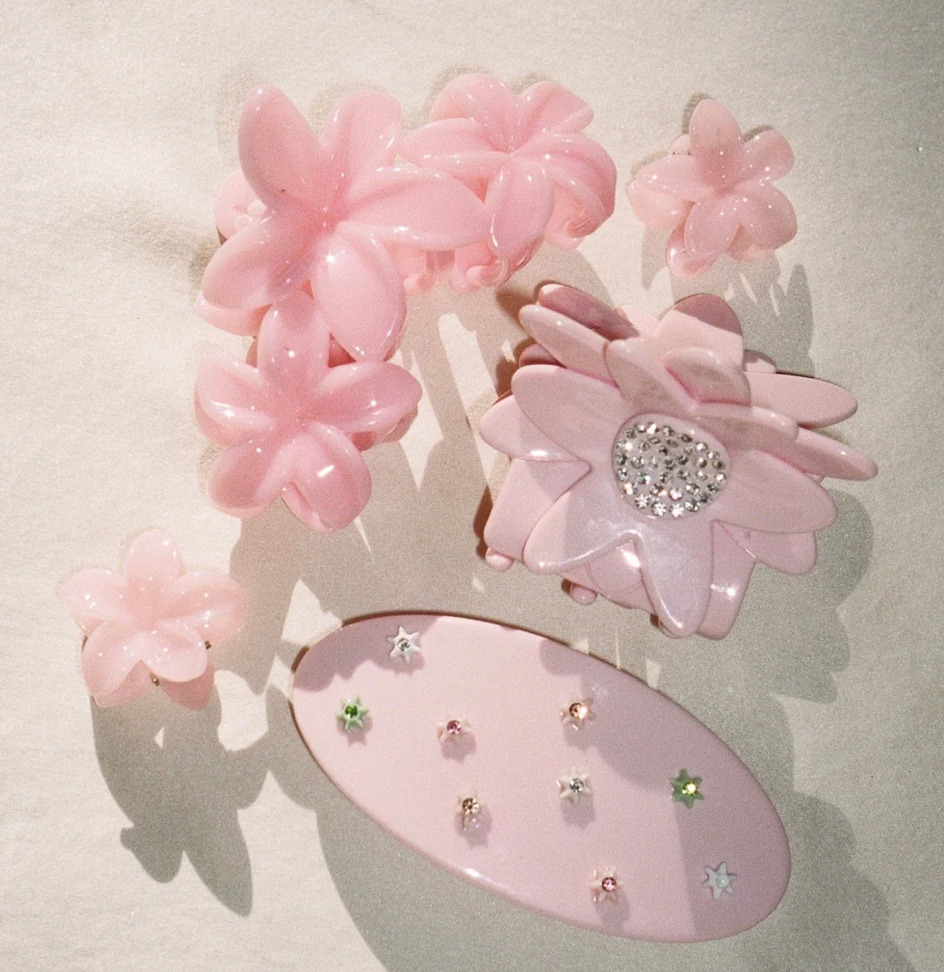 Pink resin hair clips set with flower designs and rhinestone embellishments on white background
