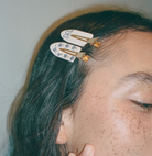 White snap hair clips with blue floral crystals and gold tone accents clipped in dark teal hair