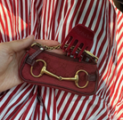 Red canvas shoulder bag with gold horsebit hardware and hair comb accessory held against red and white striped shirt