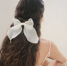 Large white fabric bow hair clip with flowing ribbons secured in brunette wavy hair, half-up hairstyle
