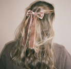 Pink velvet hair bow with long ribbon tails clipped in blonde wavy hair, worn at back of head