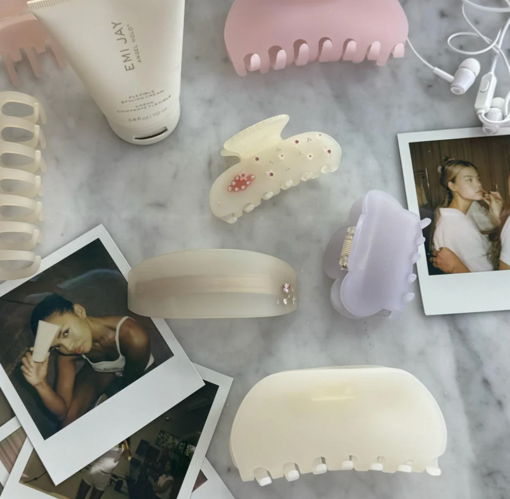 Assorted hair claw clips in cream, pink, and lavender with pearl embellishments displayed on marble surface with photos