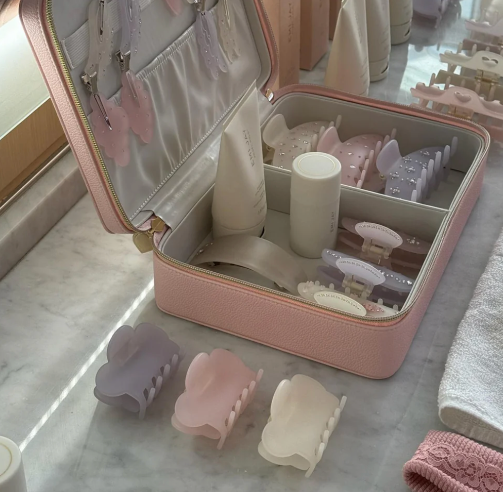 Pink faux leather travel cosmetic case with compartments containing hair clips, brushes, and beauty accessories in pastel colors