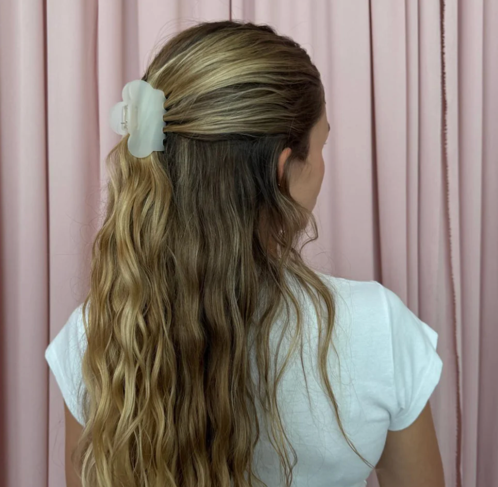Mint green flower hair claw clip securing half-up hairstyle on long wavy blonde hair against pink curtain backdrop