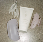 EMI JAY spa set with white tube cream and three pink quartz gua sha massage tools on speckled surface