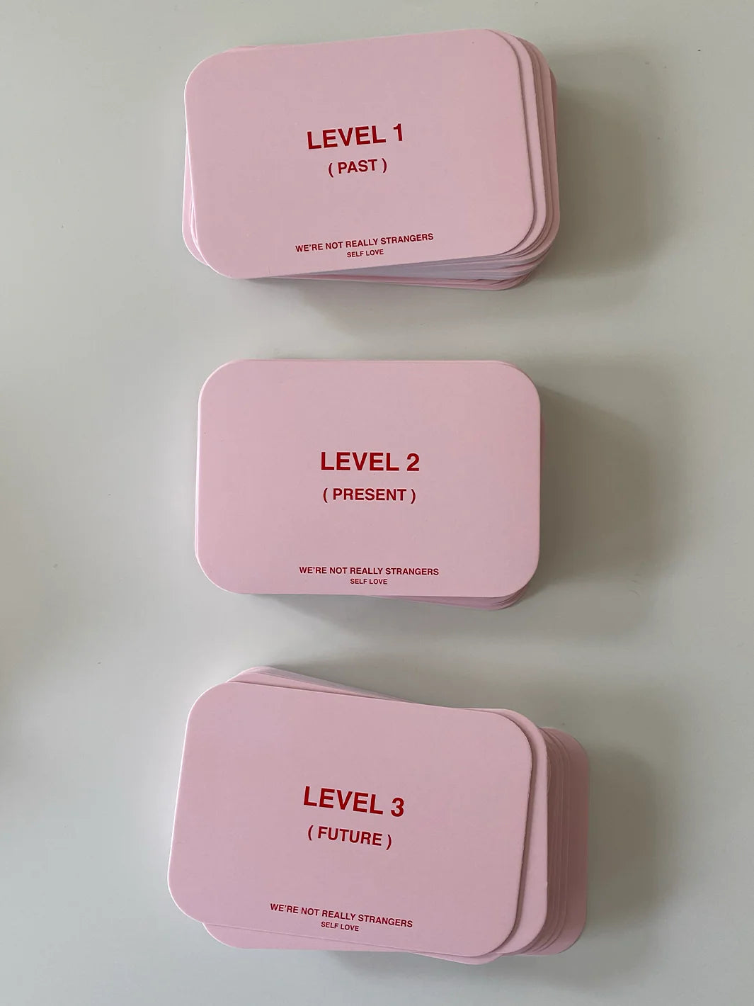 Pink card game deck with three levels - Past, Present, and Future - branded We're Not Really Strangers Self Love edition