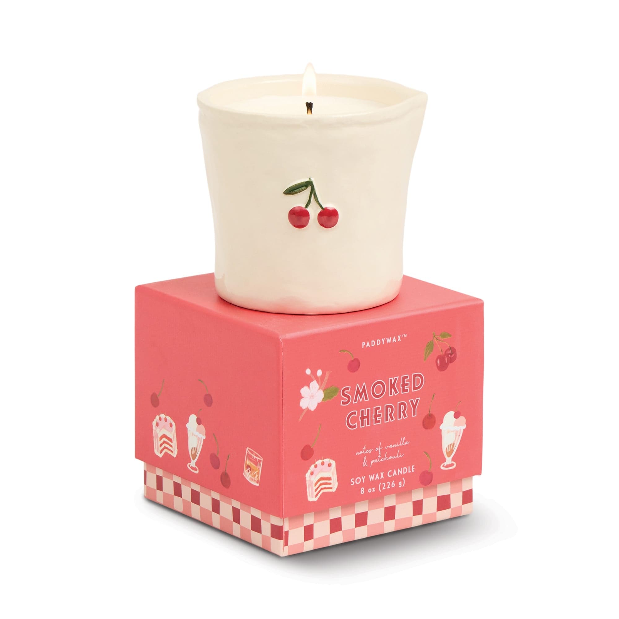 Cream-colored soy wax candle with cherry illustration on white ceramic vessel, displayed on coral pink gift box with checkered pattern
