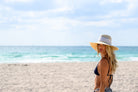 Woman in a bikini and sun hat on a beach with ocean and sky in the background