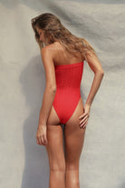 Woman wearing a red strapless swimsuit against a neutral background