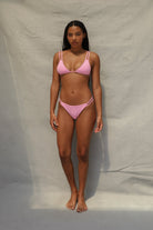 Pink two-piece bikini with triangle top and strappy bottom detail on white background