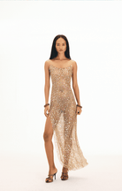 Gold sequined mesh maxi dress with spaghetti straps and high slit, worn with strappy heels and chain bracelets