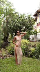Woman in gold sequined maxi dress with high slit and thin straps standing in lush garden setting