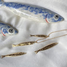 Gold fish pendant necklaces displayed on white fabric with blue and white ceramic fish decorations