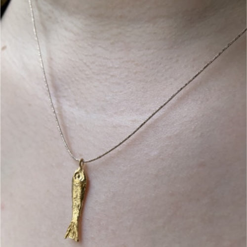 Gold fish pendant on silver chain necklace displayed on white mannequin neck