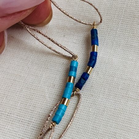 Delicate gold chain necklace with turquoise and navy blue beaded bar pendants on cream fabric background