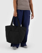 Black canvas tote bag with double handles held by person wearing navy pants and gray top